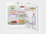Open koelkast gevuld met diverse voedingsmiddelen, waaronder groenten, fruit, yoghurt, zalm, eieren, een potje mosterd, een fles Vittel-water en een glazen fles.